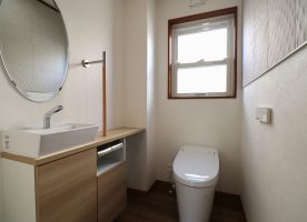 キャビネットの対面壁に設置されたエコカラットのベージュと清潔感のあるオフホワイトのトイレとが清潔感のある空間に。
